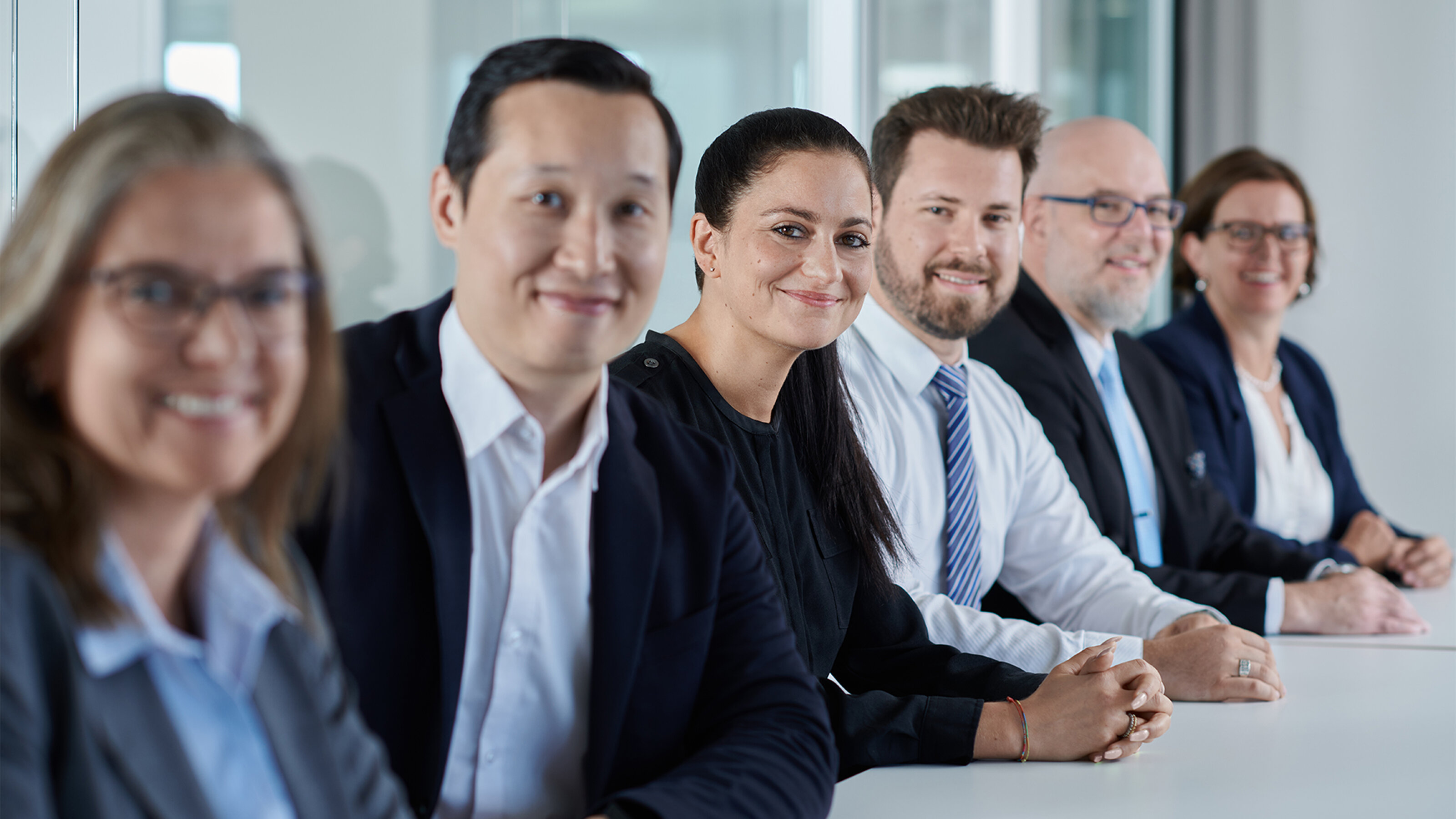 6 Sateco employees of different age, gender and origin sit next to each other at a table